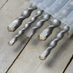 les perceuses avec des forets à percussion à pointe de carbure se trouvent dans un boîtier en plastique sur un fond en bois de planche. fermer.